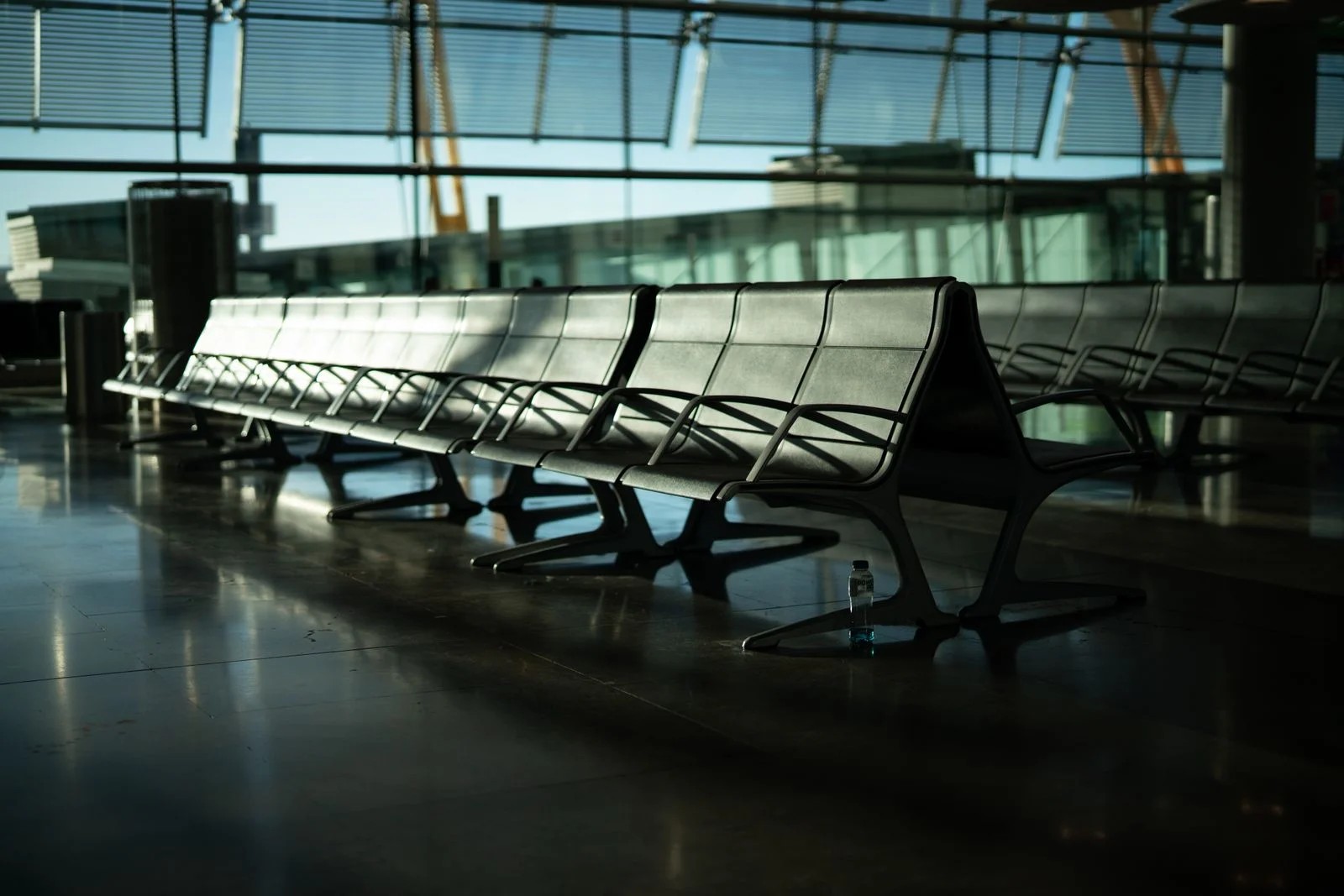 Fileira longa de poltronas metálicas vazias em sala de embarque de aeroporto, com luz do fim do dia entrando pelas janelas de vidro