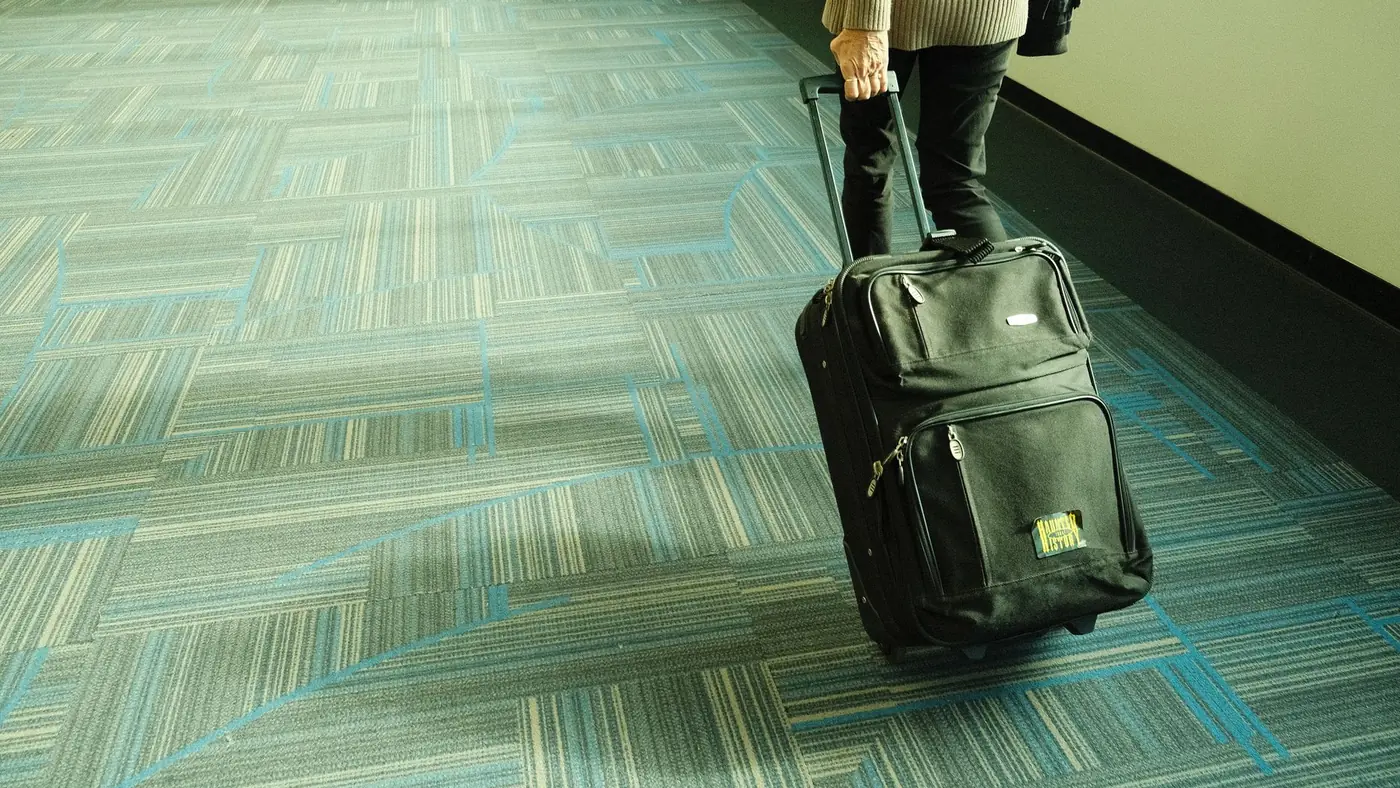 Passageiro caminhando com uma mala de rodinhas pelo corredor do aeroporto