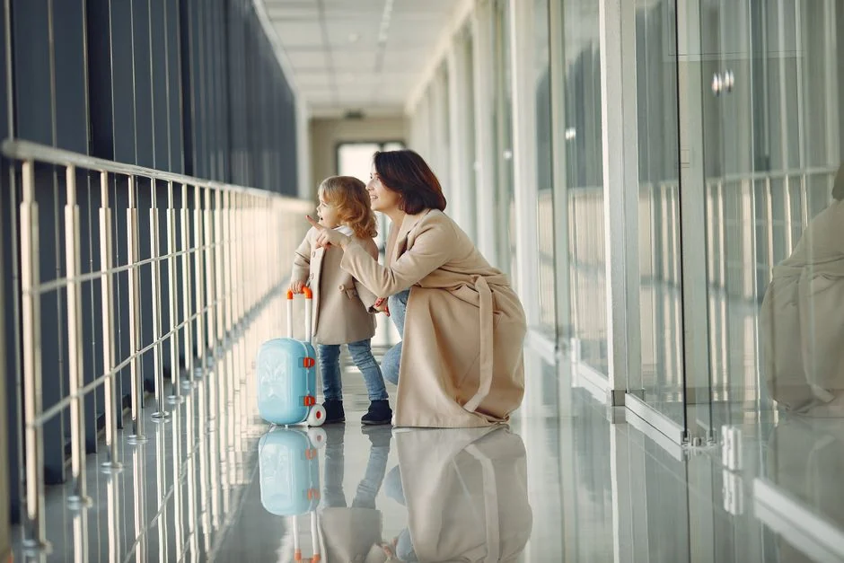 Criança pequena com mala de rodinhas ao lado da mãe em um corredor de aeroporto
