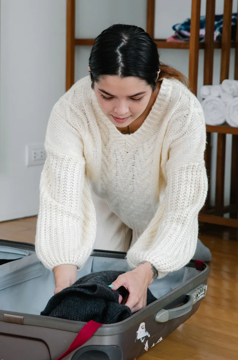 Mulher arrumando roupas dentro de uma mala aberta