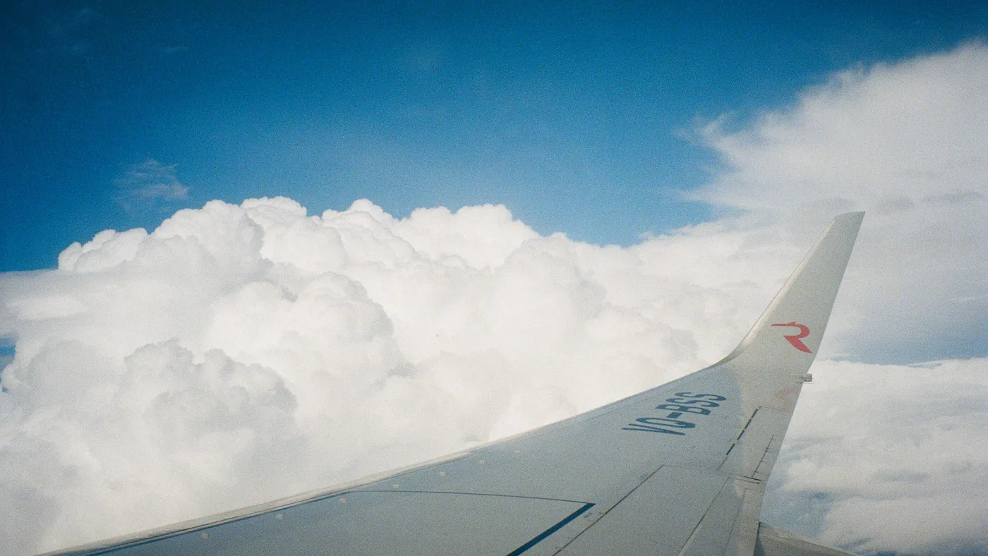 Vista pela janela do avião mostrando a asa sobre um tapete de nuvens brancas