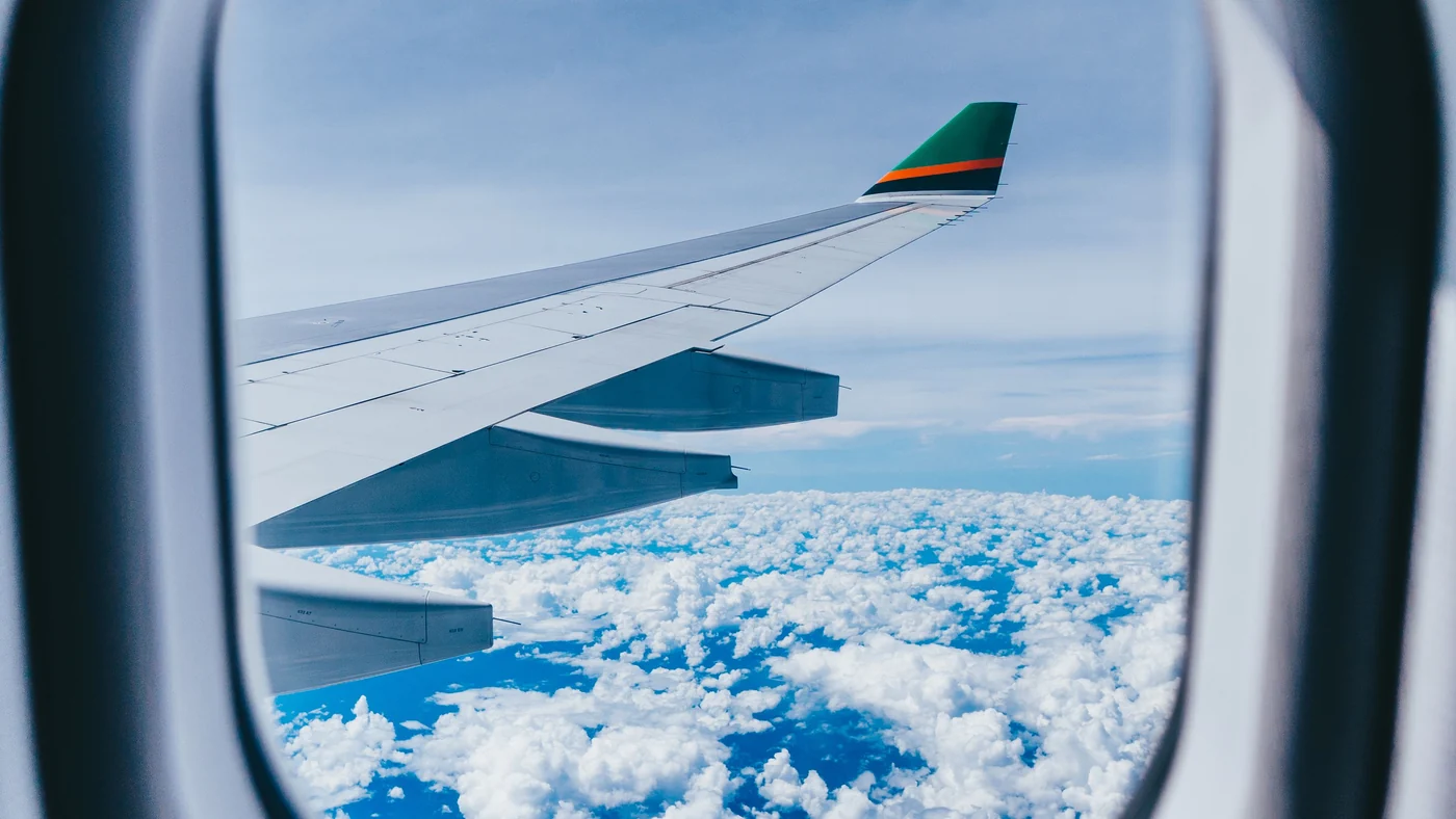 Vista pela janela do avião mostrando a asa sobre nuvens brancas durante o voo