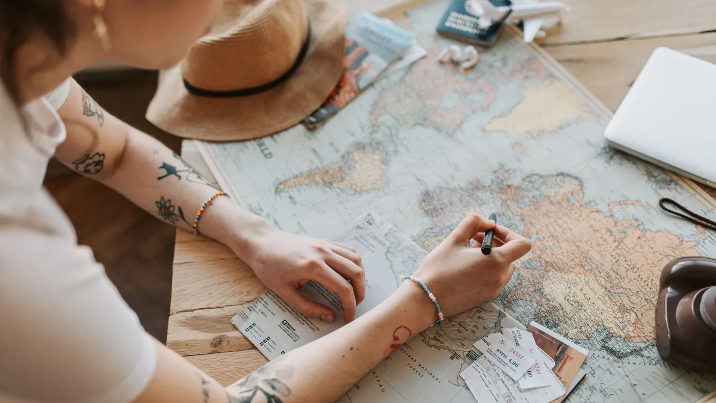 Pessoa planejando uma viagem sobre a mesa, com mapa-múndi, caneta e itens de viagem