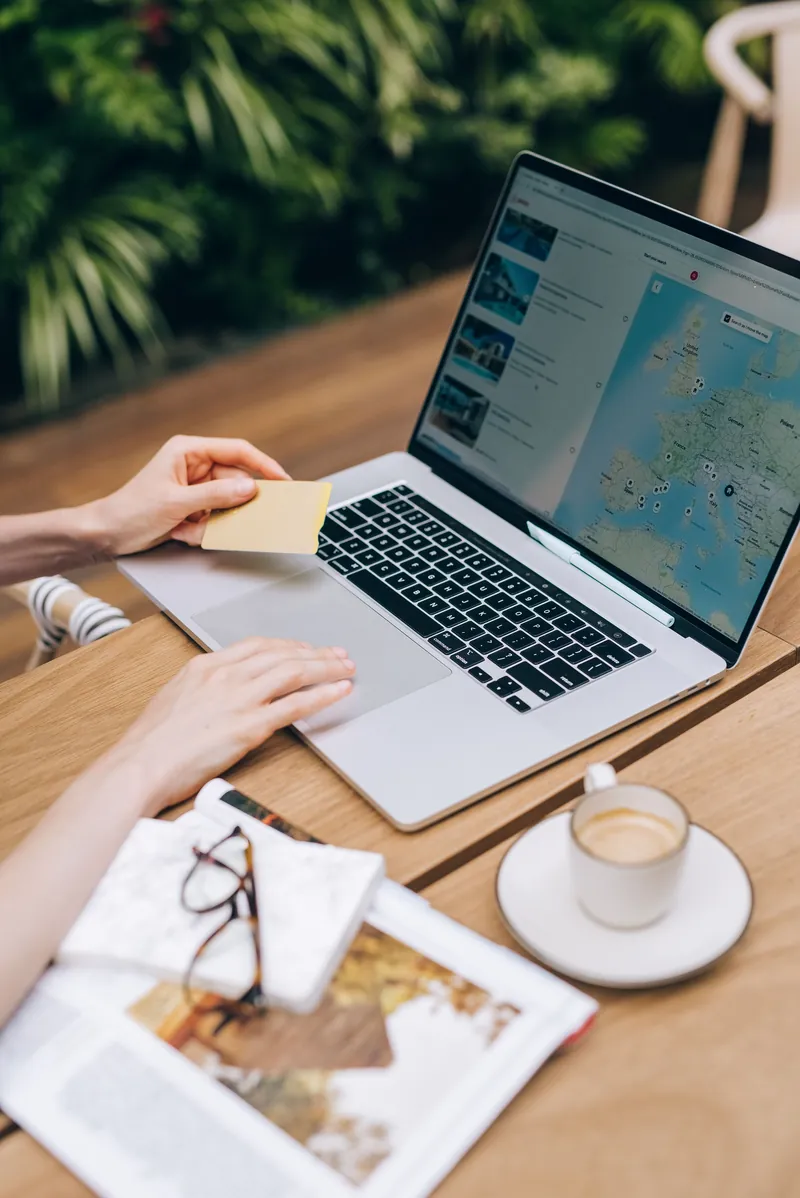 Mãos de uma pessoa segurando um cartão ao lado de um notebook aberto com um mapa da Europa na tela, sobre uma mesa de madeira