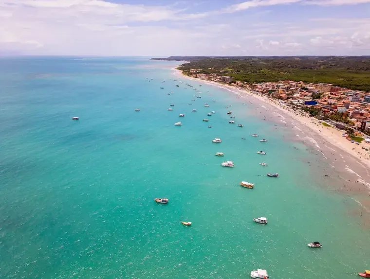 Orla de Maceió com mar verde-esmeralda, coqueiros e jangadas