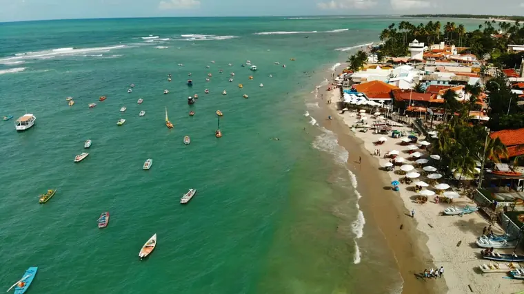 Vista aérea da praia de Porto Seguro com barcos no mar verde e barracas na areia
