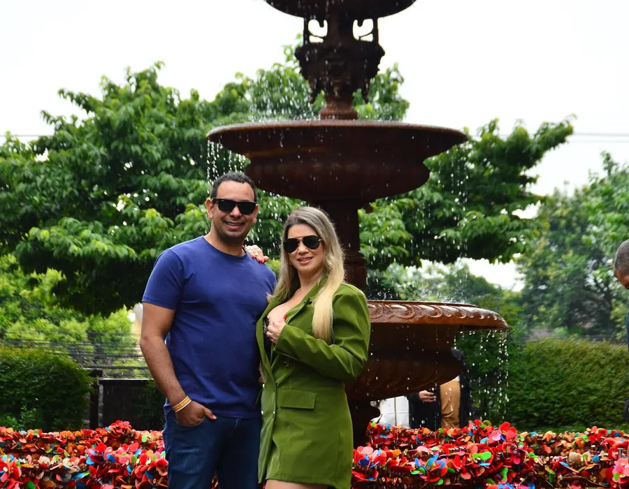 Casal de viajantes em frente a uma fonte cercada de flores em Gramado