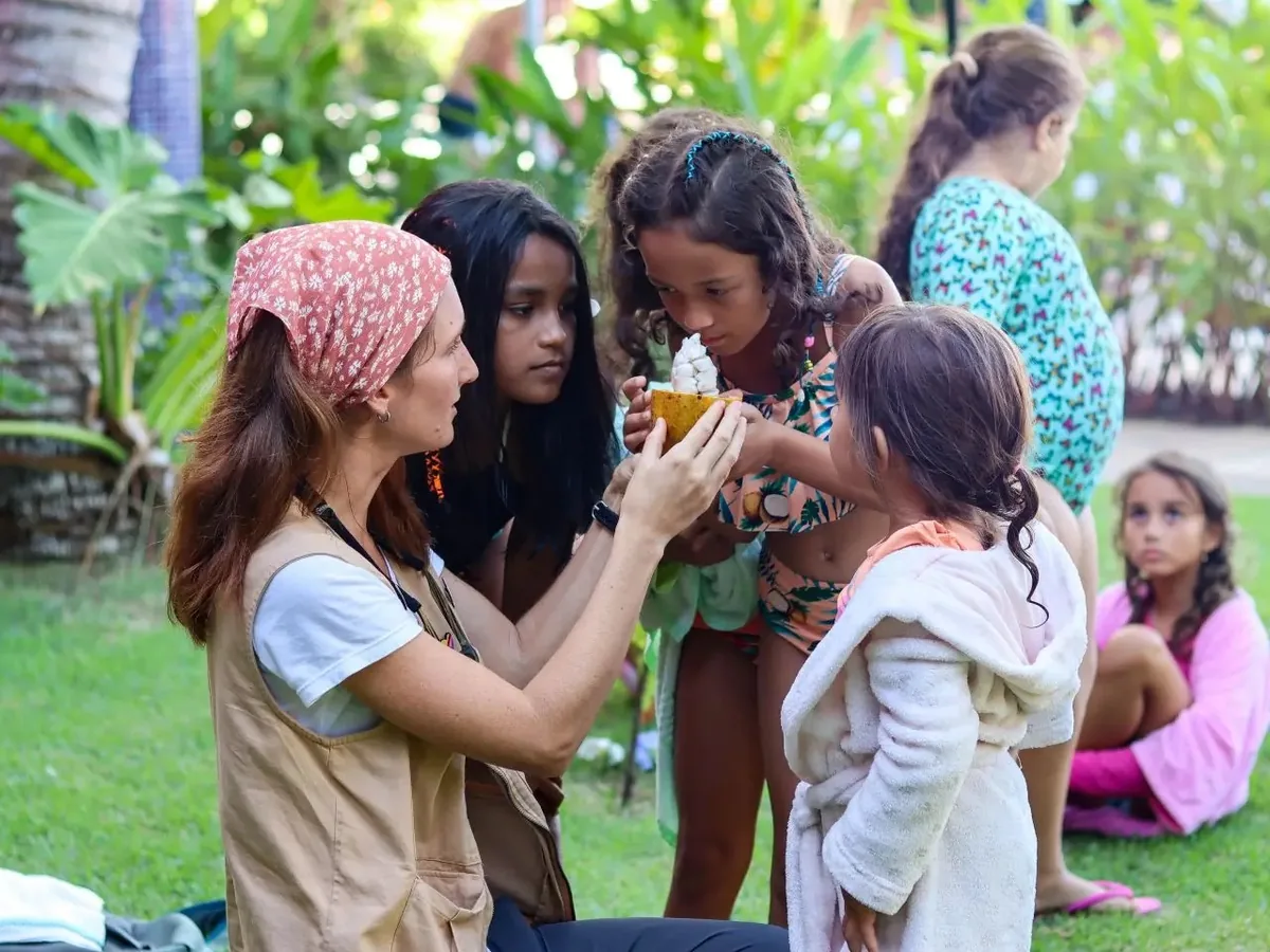 Monitora mostrando uma fruta aberta a um grupo de crianças no jardim do Resort Arcobaleno