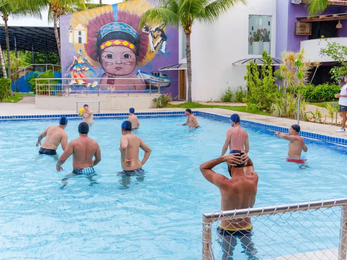 Hóspedes jogando bola na Piscina Recreativa do Resort Arcobaleno, com um mural colorido ao fundo