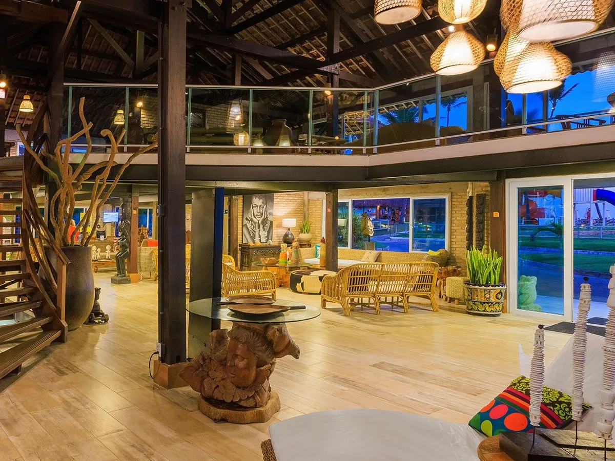 Lobby do Armação Resort, com teto de madeira, luminárias de palha, sofás e o mezanino