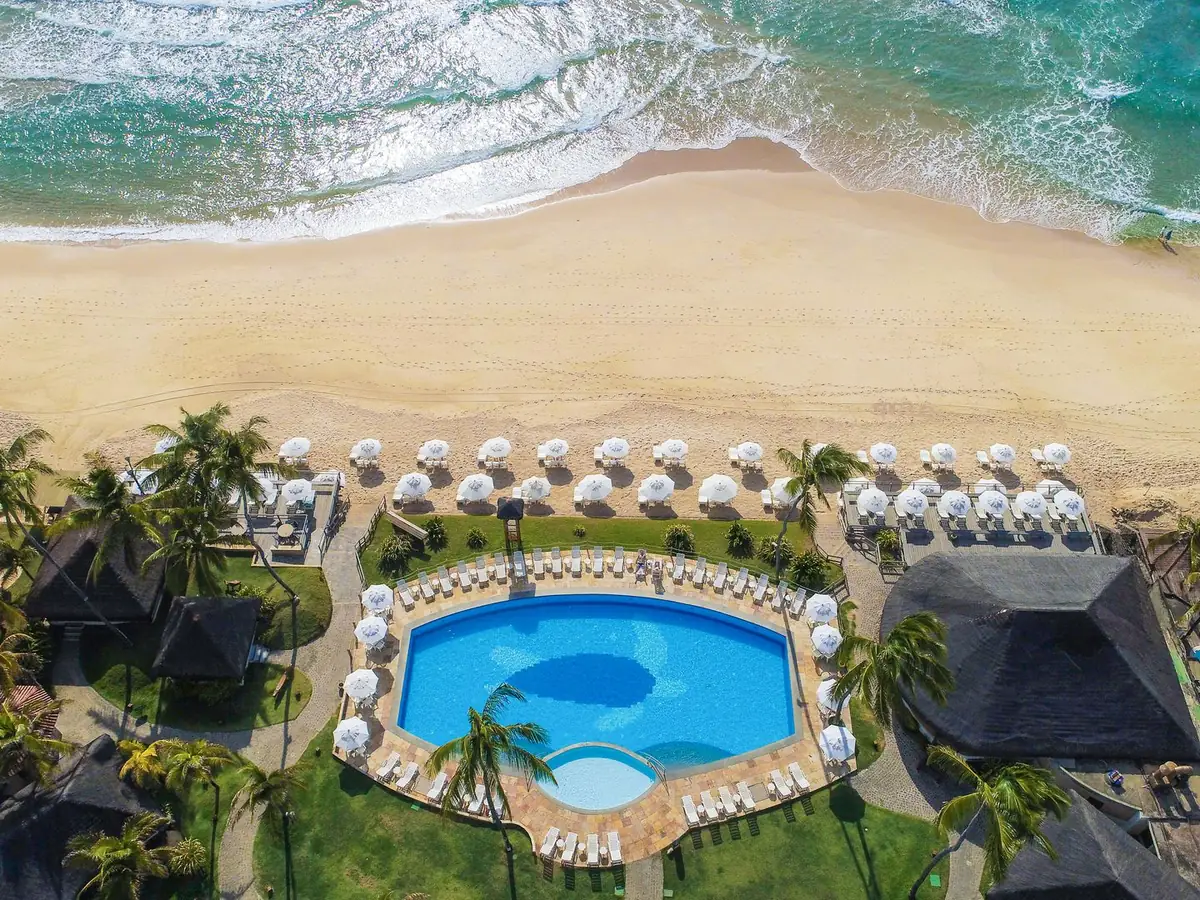 Vista aérea da piscina do Armação Resort, com guarda-sóis na areia e o mar de Porto de Galinhas em frente