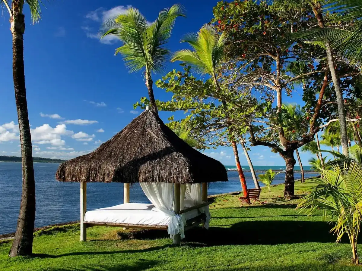 Gazebo de palha com cama de descanso no gramado à beira do rio Buranhém