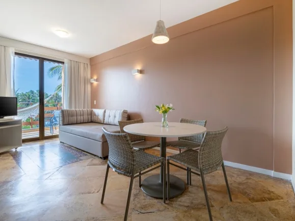 Sala de uma Suíte Júnior do Suites Beach Park, com sofá, mesa de jantar e a varanda ao fundo