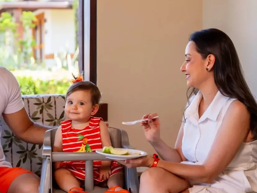 Mãe dando fruta a um bebê sentado na cadeirinha, na Baby Copa do Cana Brava Resort