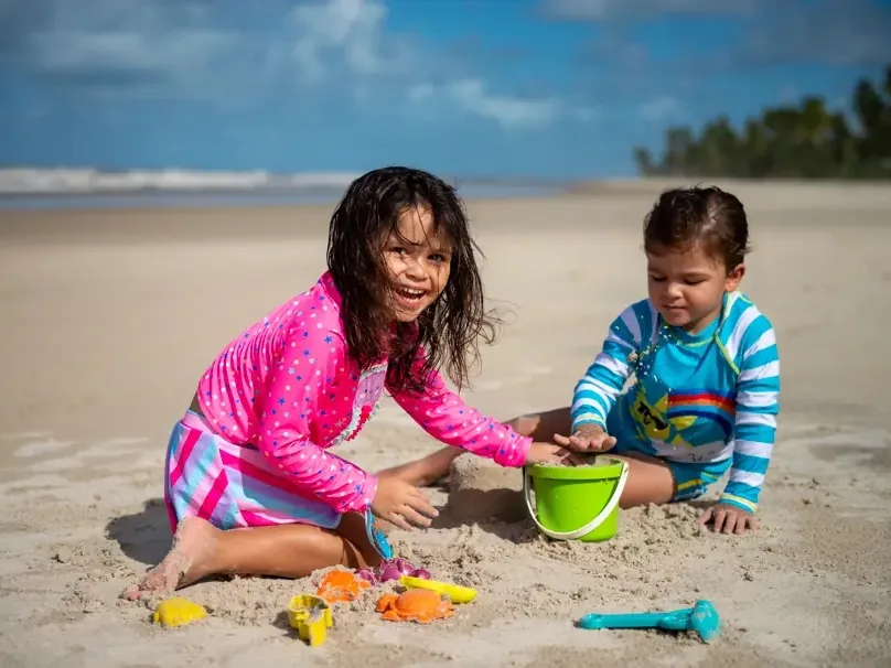 Duas crianças brincando com baldinho e forminhas na areia da praia