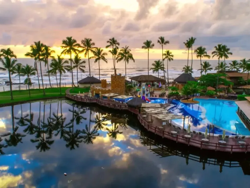 Piscinas do Cana Brava Resort ao entardecer, com o lago em primeiro plano, os coqueiros e o mar ao fundo