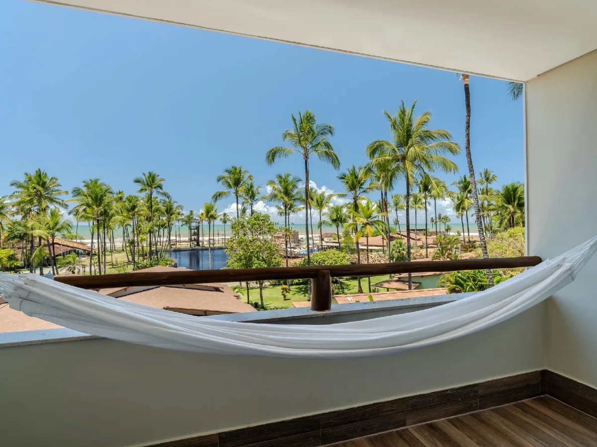 Varanda de um apartamento do Cana Brava Resort, com rede e vista para o coqueiral e o mar