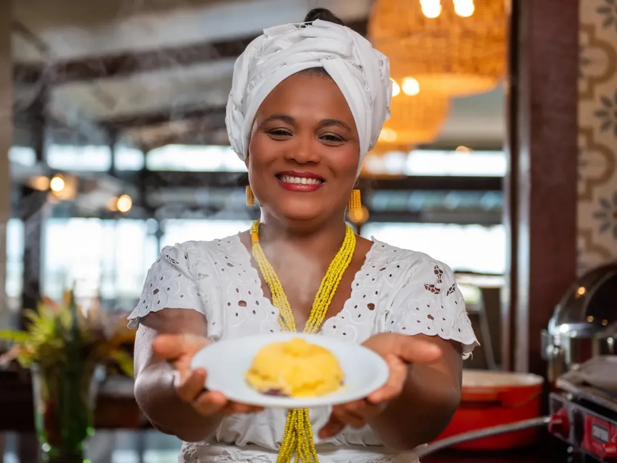 Baiana de turbante mostrando um prato no restaurante Encontro das Águas do Cana Brava Resort