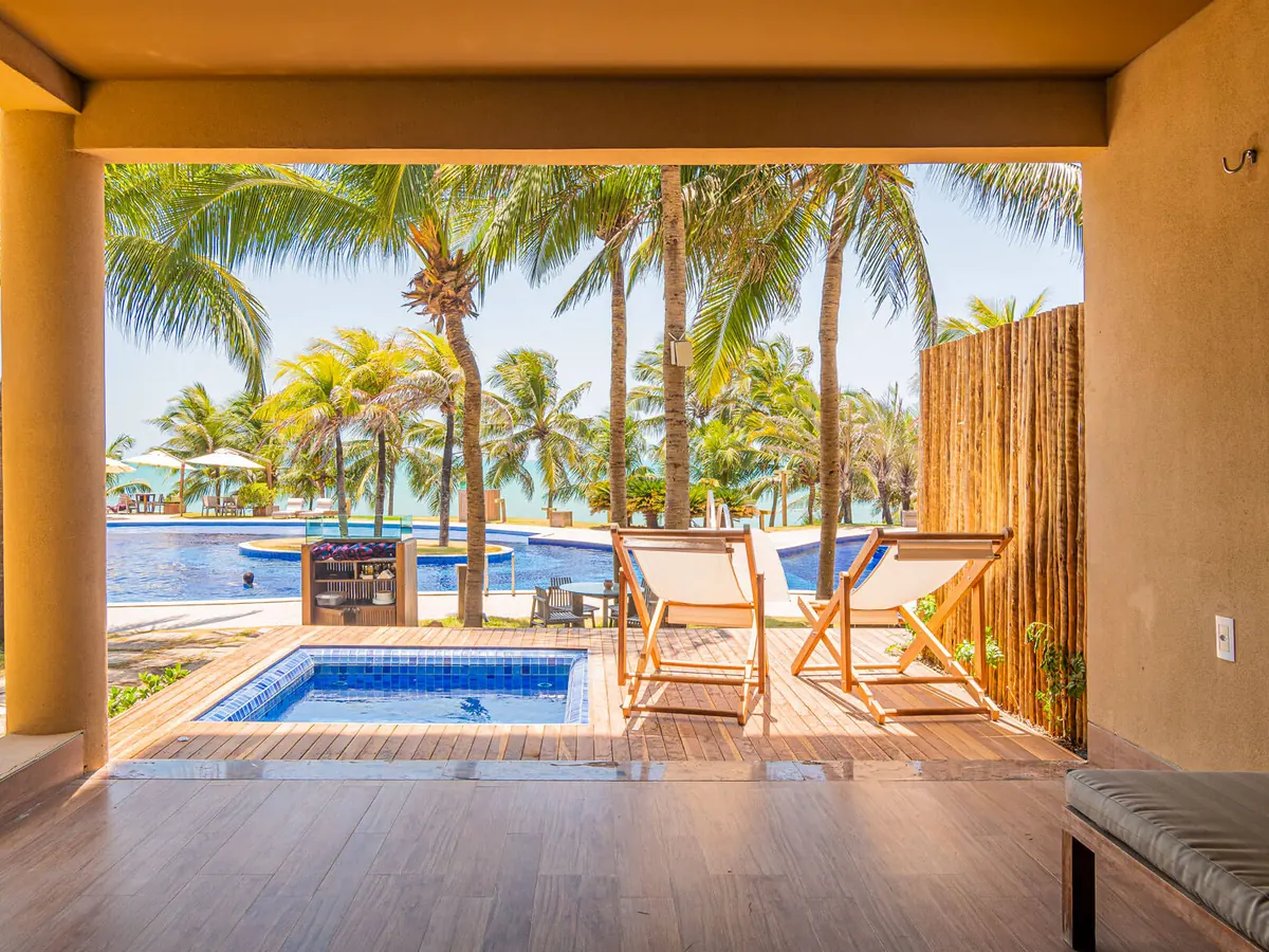 Varanda da Suíte Premium com Hidro do Carmel Charme Resort, com a hidro, duas cadeiras de lona e a piscina e o mar ao fundo