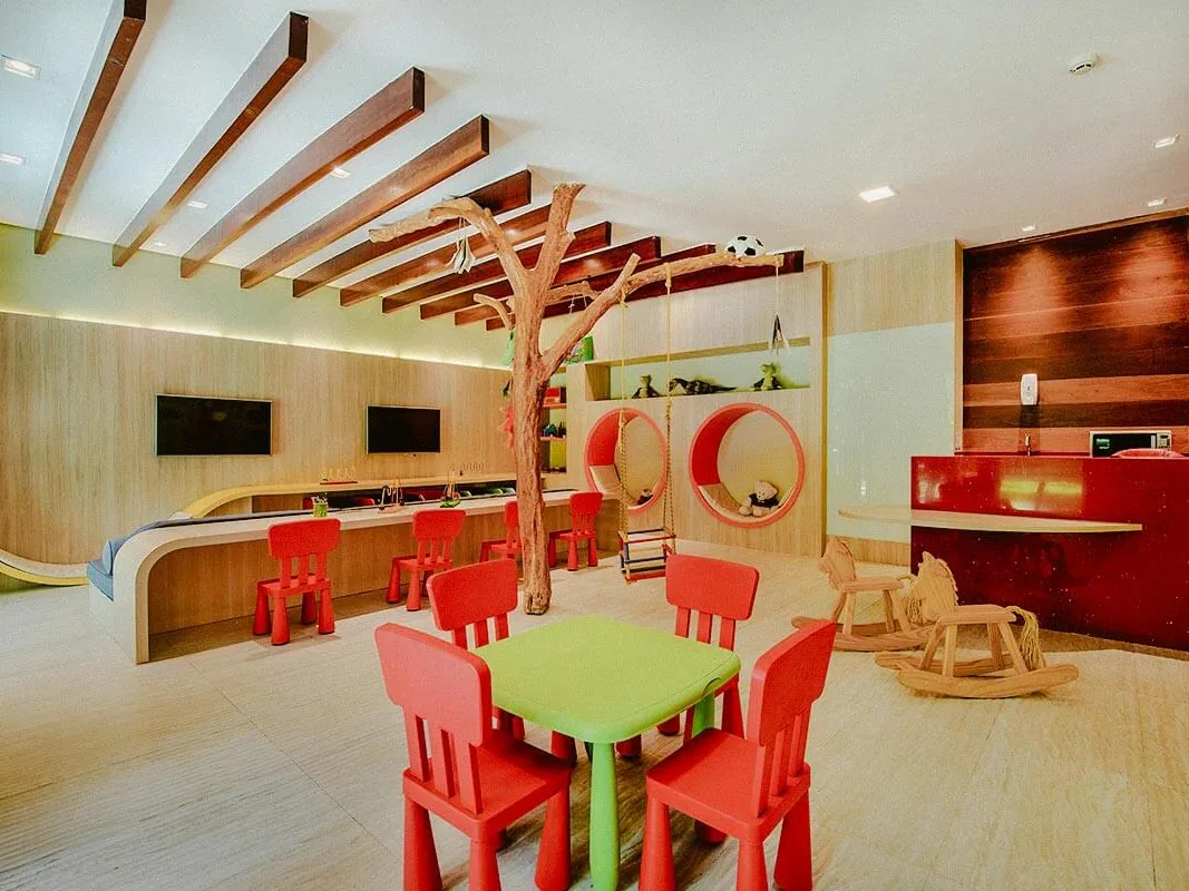 Espaço infantil Carmelzinho, com mesinhas vermelhas, cavalinhos de balanço e uma árvore decorativa