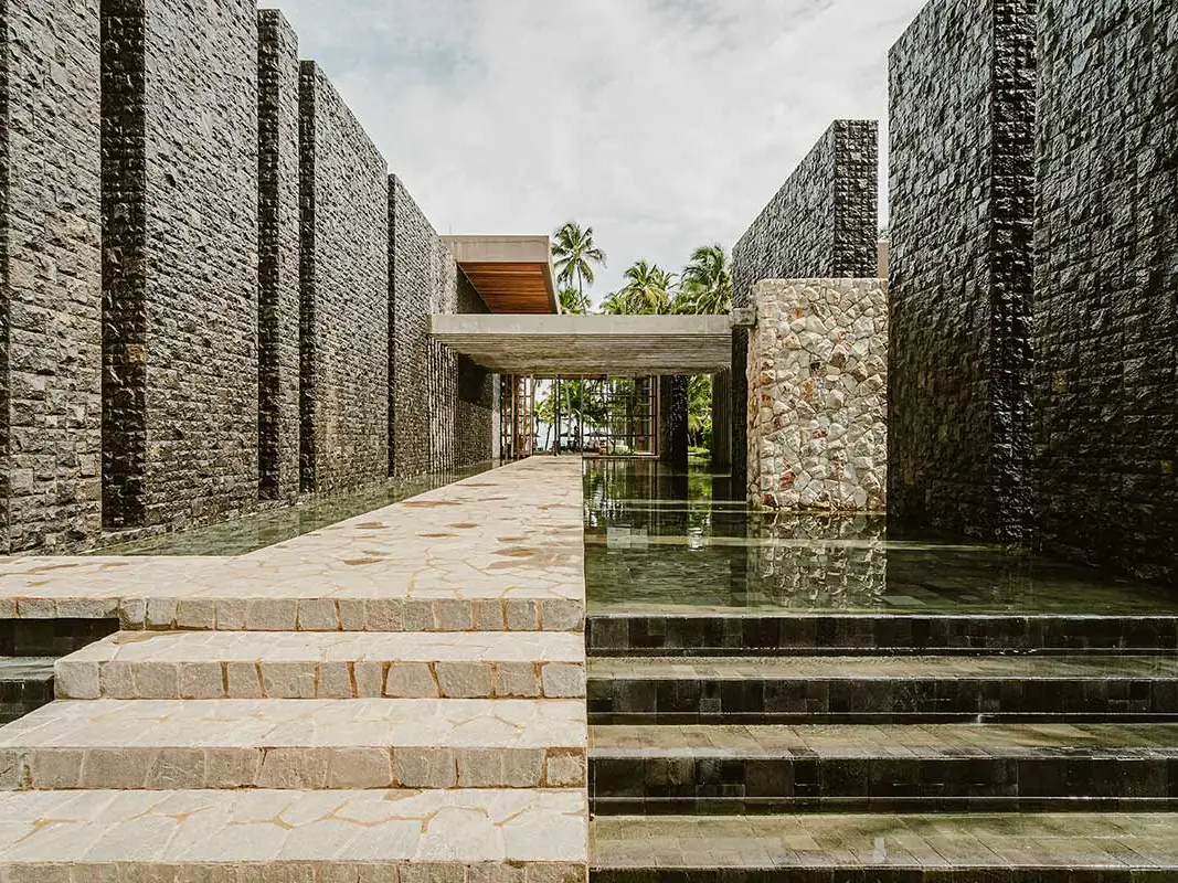 Entrada do Carmel Taíba, com escadaria de pedra entre muros escuros e espelho de água