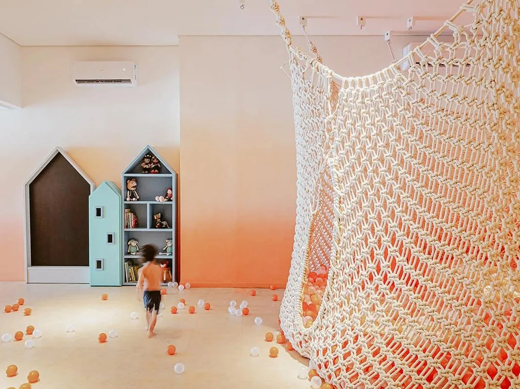 Espaço infantil Carmelzinho, com rede de escalada, estantes em forma de casinha e bolinhas coloridas no chão