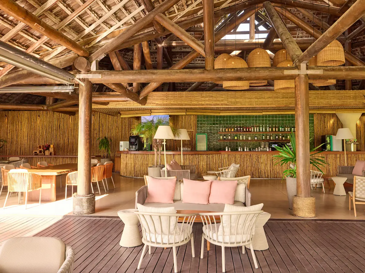 Lounge do Bar Principal do Club Med Trancoso, com sofás de almofadas rosa e o balcão sob o telhado de madeira