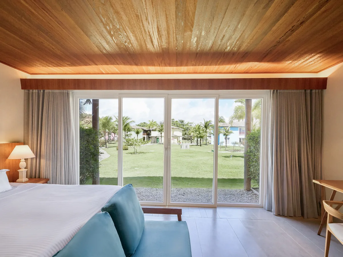 Quarto Superior Familiar Novo do Club Med Trancoso, com cama de casal, sofá azul e porta de vidro para o gramado