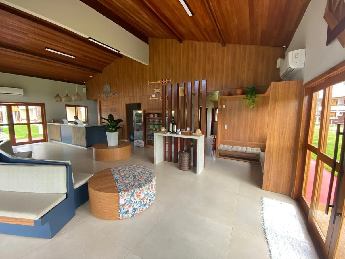 Recepção e área de estar do Coroa Vermelha Beach, com sofás, pufes e paredes de madeira