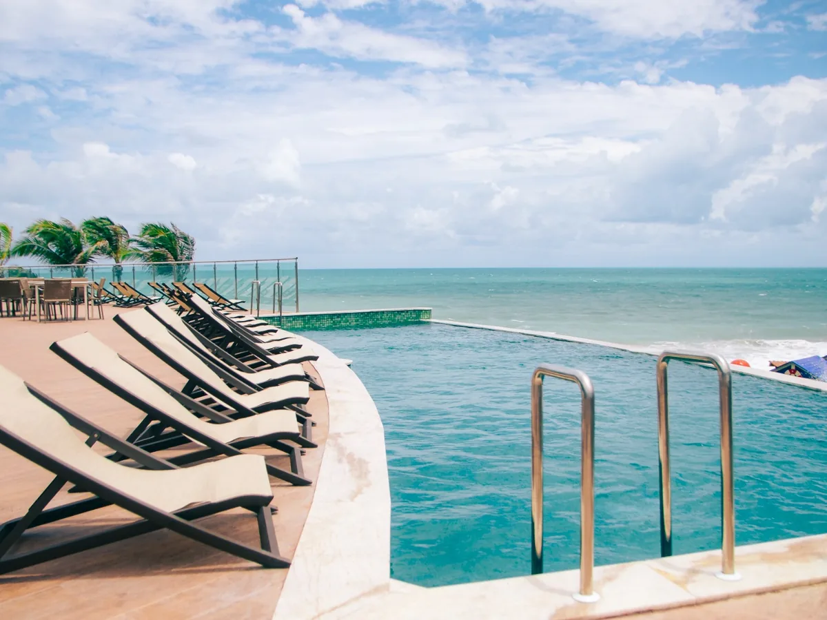 Piscina de borda infinita do Costeira Palace com espreguiçadeiras no deque e o mar ao fundo