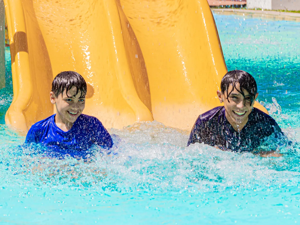 Dois meninos descendo o escorregador amarelo na piscina do El Aram Imirá