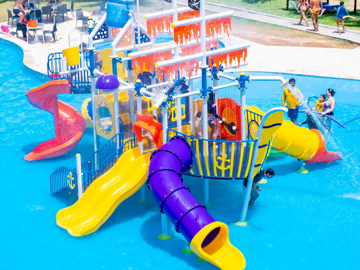 Parque aquático infantil do El Aram Imirá, com escorregadores coloridos e crianças brincando na piscina