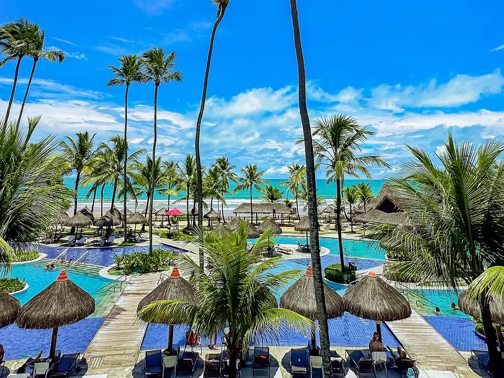 Piscinas do Enotel Porto de Galinhas com quiosques de palha e coqueiros, e o mar ao fundo