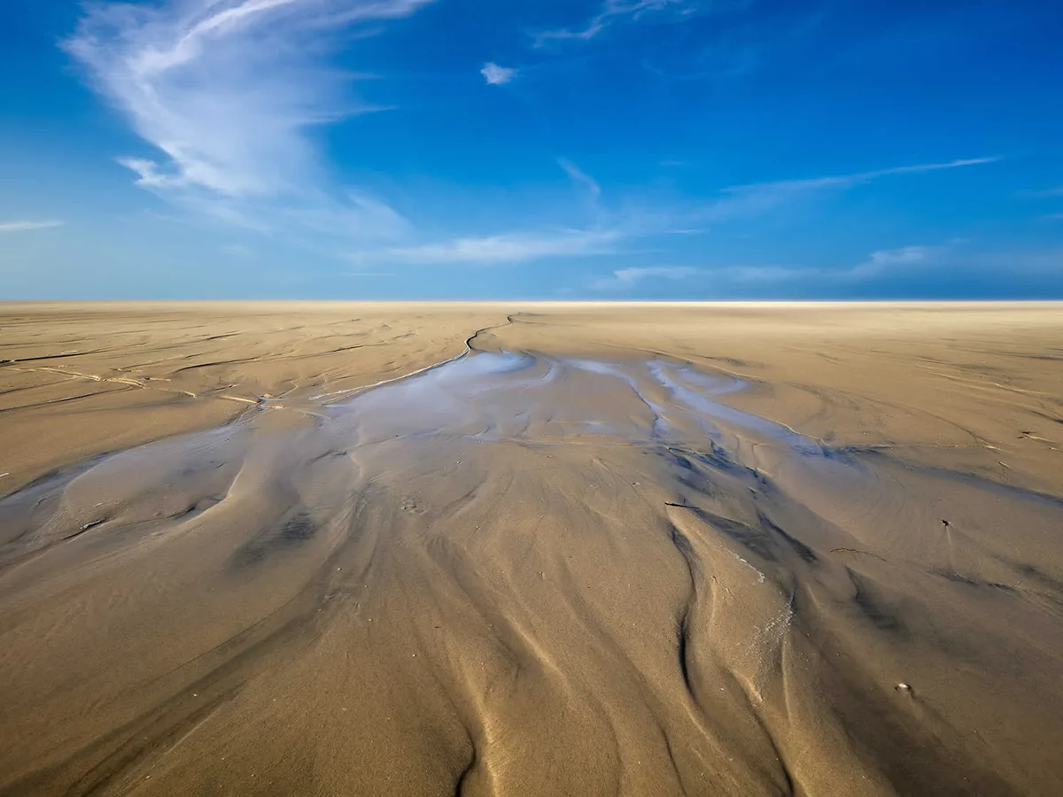 Praia de Jericoacoara na maré baixa, com a areia molhada e o céu azul