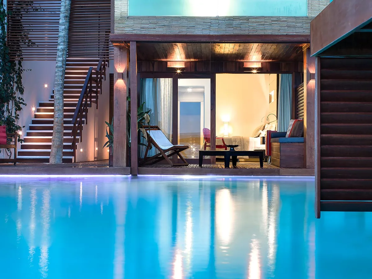 Apartamento Essenza Lounge aberto para a piscina ao anoitecer, com espreguiçadeira na varanda e escada iluminada ao lado