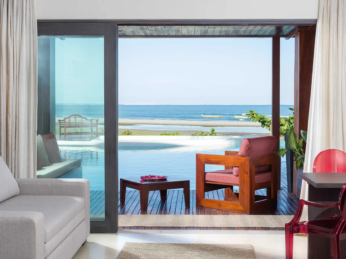 Sala de um apartamento do Essenza Hotel aberta para o deque, com a piscina de borda infinita e o mar ao fundo