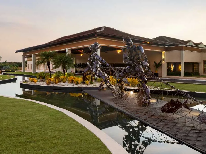 Entrada do lobby do Grand Palladium Imbassaí ao entardecer, com esculturas de pescadores puxando a rede sobre o espelho d'água