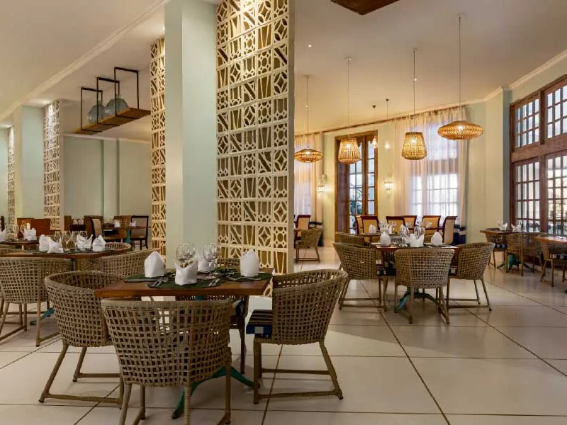 Salão do restaurante italiano Portofino, com mesas postas, cadeiras de fibra e luminárias de palha