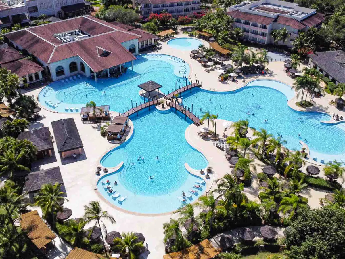 Piscina principal do Grand Palladium Imbassaí vista do alto, com pontes de madeira, coqueiros e os prédios em volta