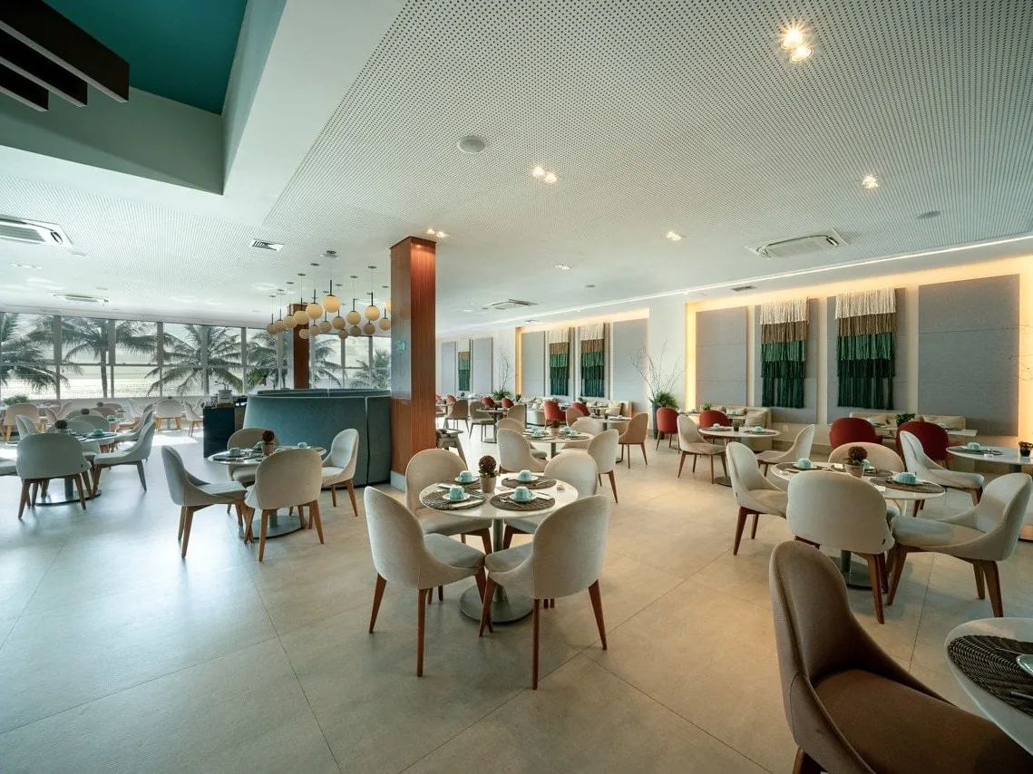 Salão de restaurante do Japaratinga Lounge Resort, com mesas redondas e janelas de vidro para os coqueiros