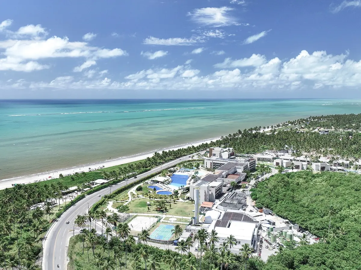 Vista aérea do Japaratinga Lounge Resort, com as piscinas, os coqueiros e o mar verde de Japaratinga