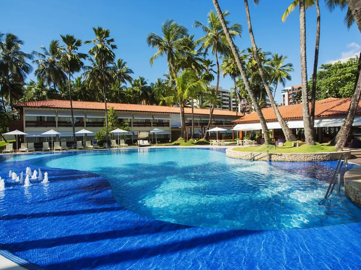 Piscina do Jatiúca Resort com jatos d'água, coqueiros e o bloco de apartamentos ao fundo