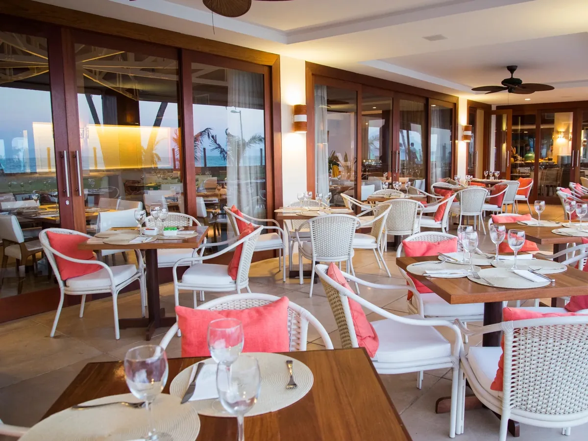 Salão do restaurante Canoas, do Jatiúca Resort, com mesas postas e o mar visto pelas portas de vidro