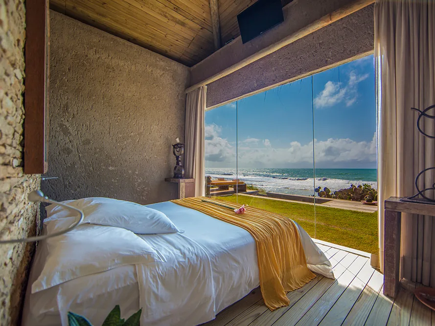 Suíte do Kenoa Resort com cama de casal e janela de vidro de frente para o mar
