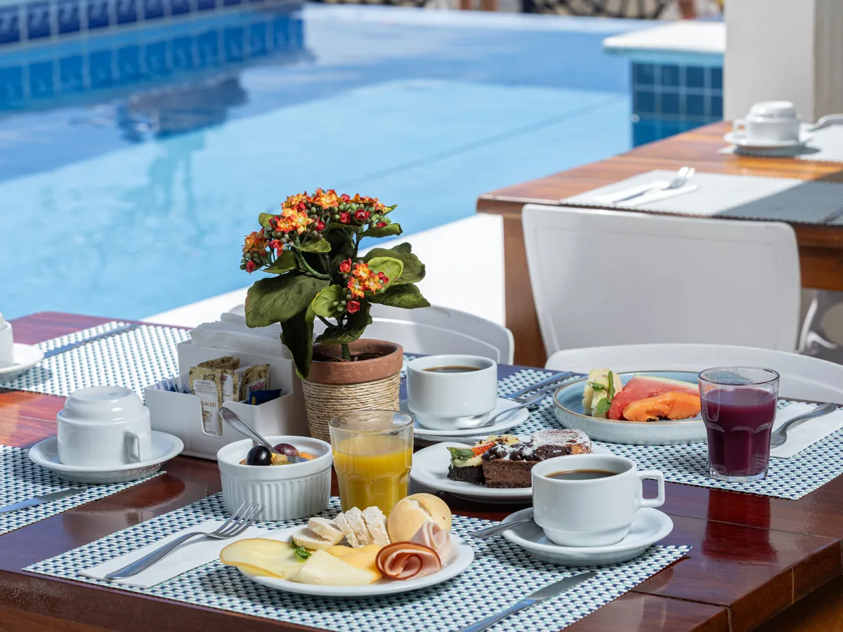 Mesa de café da manhã do SERHS Beach Hotel com frutas, frios, bolo, suco e café, ao lado da piscina