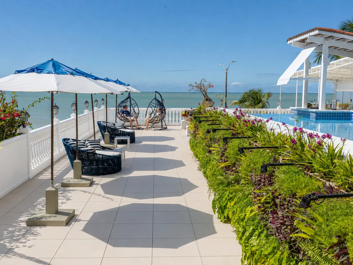 Terraço do SERHS Beach Hotel com poltronas, guarda-sóis e cadeiras suspensas, a piscina e o bar à direita e o mar ao fundo