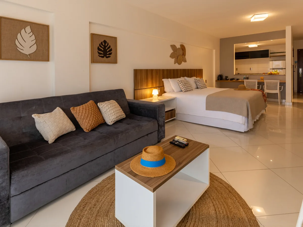 Studio do SERHS Beach Hotel com sofá cinza, cama de casal e a cozinha americana ao fundo