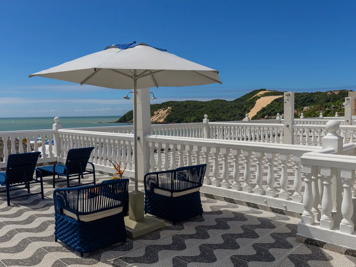Terraço do SERHS Beach Hotel com poltronas azuis, guarda-sol e o Morro do Careca ao fundo