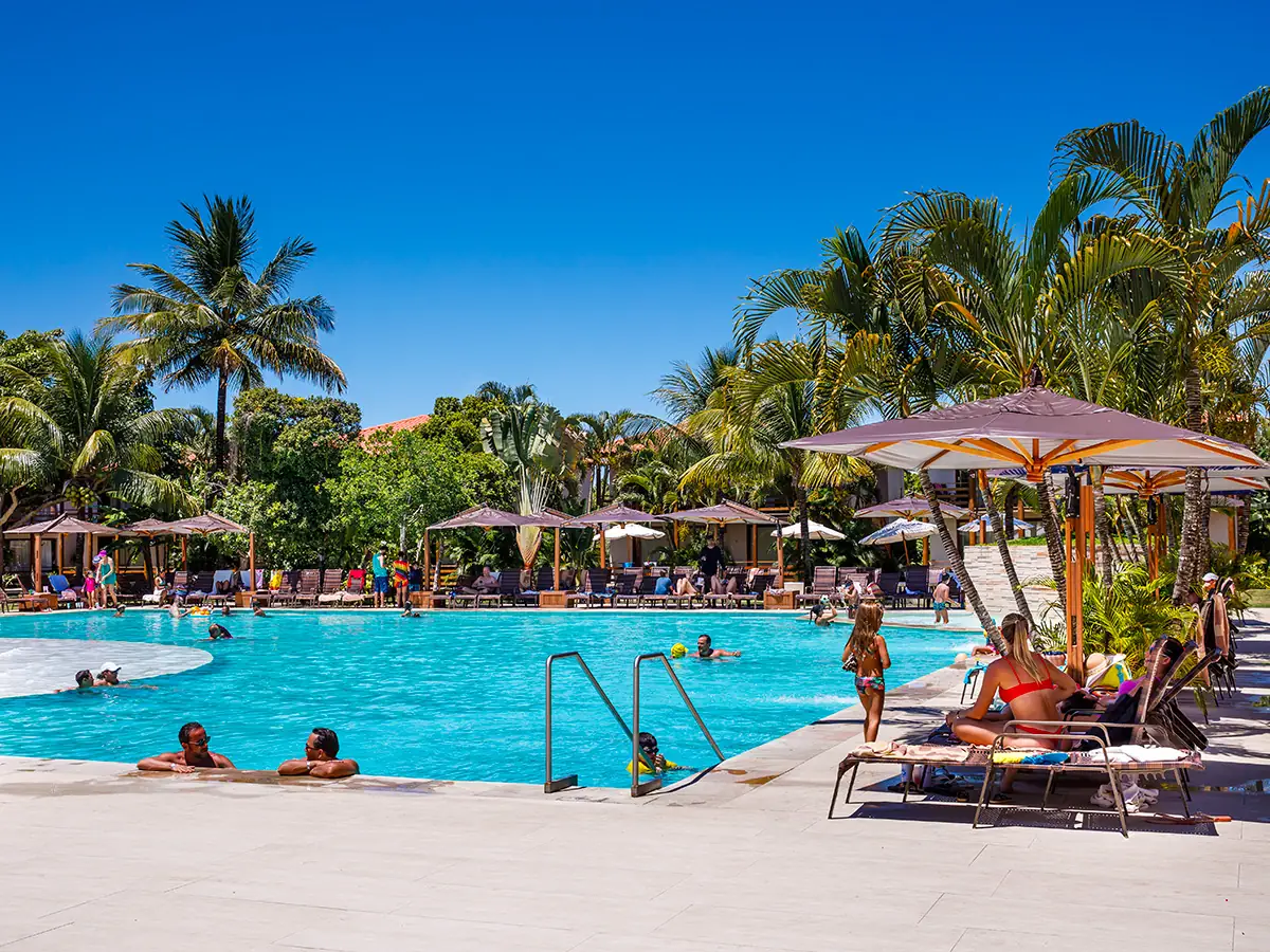 Piscina central do La Torre Resort com guarda-sóis, coqueiros e hóspedes na borda