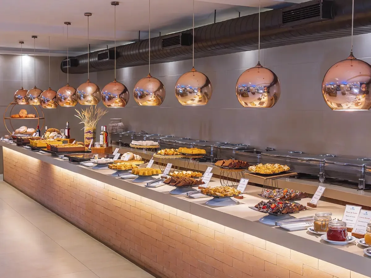 Bufê de doces e pães no restaurante do La Torre Resort, sob luminárias acobreadas